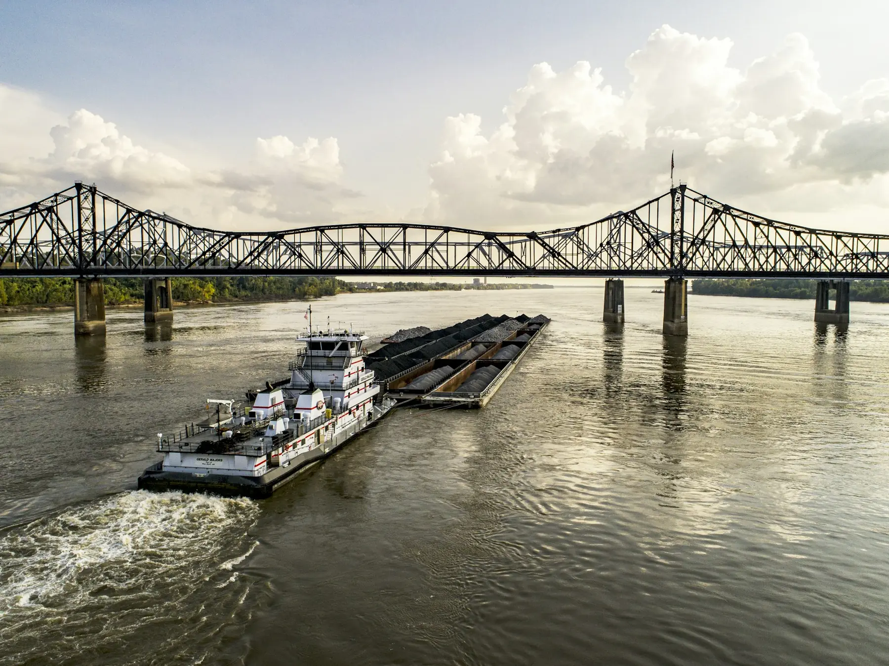 A towboat and barges passing under a steel truss bridge